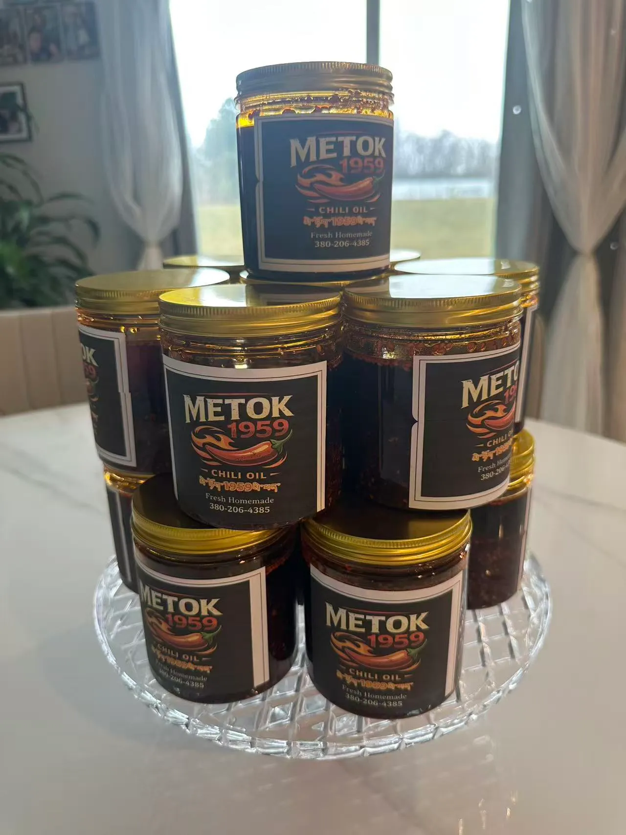 A tower of Metok 1959 chili oil jars with gold lids by a window